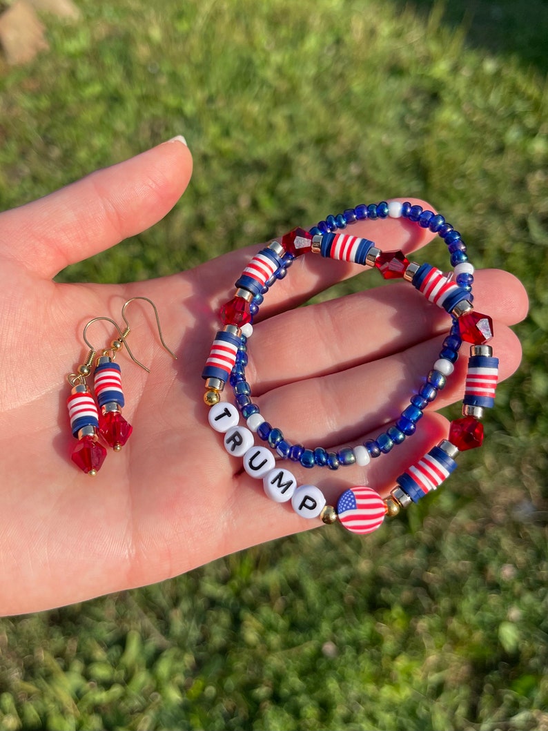 K&ouml;nnte beinhalten: Ein Set aus rot-wei&szlig;-blauen Perlen-Schmuck mit einem Armband, auf dem das Wort "TRUMP" in wei&szlig;en Perlen geschrieben ist und einem amerikanischen Flaggen-Anh&auml;nger. Das Set enth&auml;lt auch ein Paar Ohrringe mit rot-wei&szlig;-blauen Perlen.