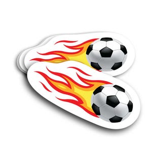 May include: Two white oval stickers featuring a soccer ball with black and white panels, trailing behind a stylized flame design in red, orange, and yellow. The stickers have a glossy finish and a white background.