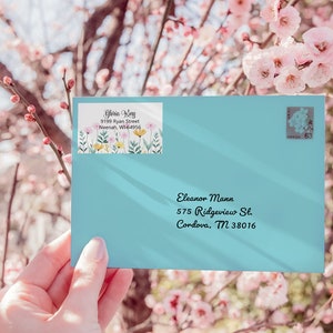 May include: A light blue envelope with a floral address label and a stamp. The address label reads "Gloria King, 9199 Ryan Street, Neenah, WI-64956". The envelope is addressed to "Eleanor Mann, 575 Ridgeview St, Cordova, TN 38016".
