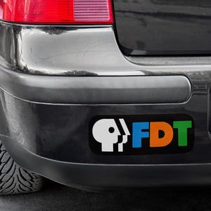 Pu&ograve; includere: Un adesivo per paraurti nero con una silhouette bianca di una testa con una scritta "FDT" blu, arancione e verde.