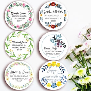 May include: A collection of six round address labels with floral designs. Each label features a name and address, surrounded by watercolor illustrations of flowers and greenery. The labels are in various colors, including pink, yellow, blue, and green.