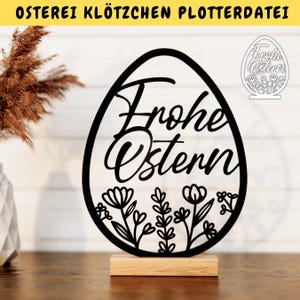 May include: Black and white silhouette of an Easter egg with the text "Frohe Ostern" and floral designs. The egg is on a wooden stand.