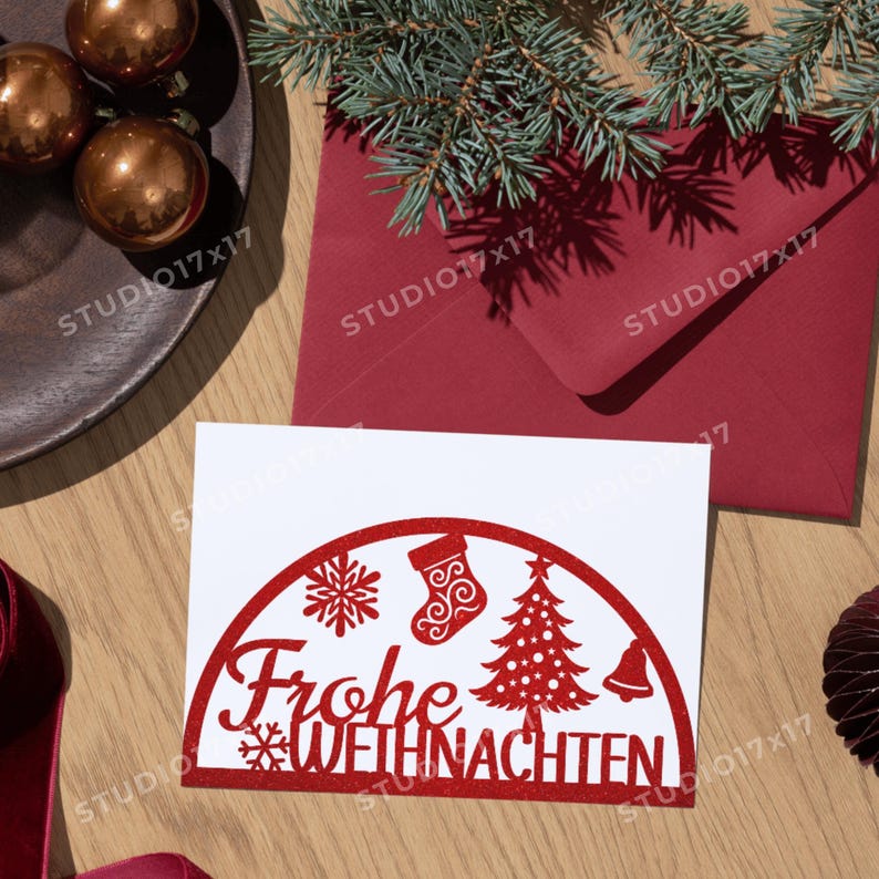 May include: A white card with a red cut-out design that says "Frohe Weihnachten" with a snowflake, stocking, Christmas tree, and bell. The card is on a wooden surface with a red envelope and pine needles.