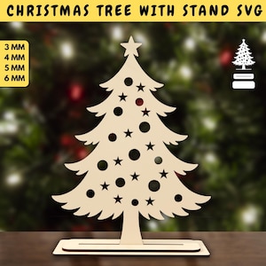 Può includere: Un albero di Natale in legno con supporto. L'albero ha una stella in cima, ritagli a forma di stella e cerchio ed è esposto su un supporto. Il testo "CHRISTMAS TREE WITH STAND SVG" è in alto. Spessori: 3 mm, 4 mm, 5 mm e 6 mm.
