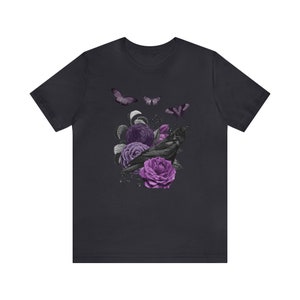May include: A dark gray t-shirt with a black crow perched on purple roses and butterflies. The crow is surrounded by purple flowers and leaves.