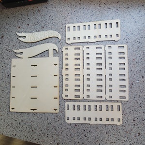 May include: A set of unfinished wooden pieces for a Hot Wheels display stand. The pieces are cut out in the shape of a car and have slots for holding cars. The pieces are labeled "Hot Wheels".
