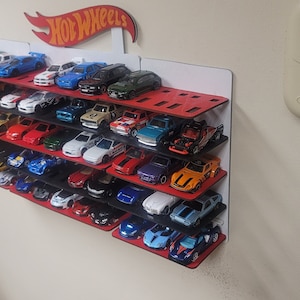 May include: A red and black wall-mounted shelf with a Hot Wheels logo holds a collection of miniature toy cars. The cars are arranged in rows on the shelves, with a variety of colors and styles.
