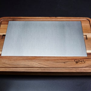 Peut inclure: Planche à découper rectangulaire en bois avec un insert en acier inoxydable. La planche a une rainure à jus sur le pourtour et une découpe de chaque côté. La marque "GIGI" est gravée dans le coin inférieur droit.