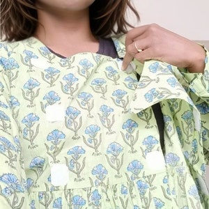 Op de afbeelding: Een vrouw draagt een lichtgroene jurk met een blauwe bloemenprint. De jurk heeft een geplooide rok en een V-hals.