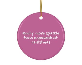 Könnte beinhalten: Runder, magentafarbener Weihnachtsschmuck mit goldener Aufhängeschnur. Der Text "Emily: more sparkle than a peacock at Christmas" ist in Weiß auf dem Ornament aufgedruckt.