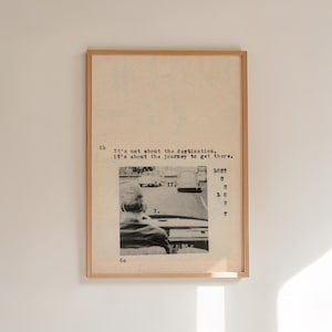 May include: A framed print with a vintage aesthetic. The artwork features a black and white photograph of a person in a car, with text overlayed. The text includes the phrases "It's not about the destination" and "LOST". The frame is a light brown colour.