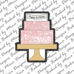 Puede incluir: Un pastel rosa y blanco con una pancarta blanca que dice "Feliz cumpleaños" en la parte superior. El pastel está sobre un soporte dorado.