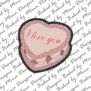 May include: A pink heart-shaped cake with white frosting and red bows. The cake is decorated with the words "I love you" in red.