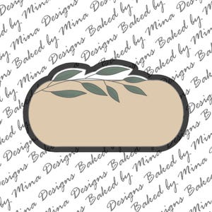 May include: A brown oval-shaped cookie cutter with a black outline and a leafy design at the top. The cookie cutter is on a white background with the text "Designs Baked by Mina" repeated.