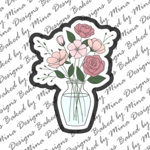 May include: A black-rimmed cookie cutter shaped like a bouquet of pink flowers in a clear glass vase. The design features several pink rose-like blossoms, small buds, and green leaves arranged in a vase with visible stems inside the glass.