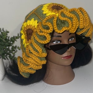 May include: A crocheted sunflower hat with green and yellow yarn. The hat has a ruffled edge and is decorated with crocheted sunflowers.