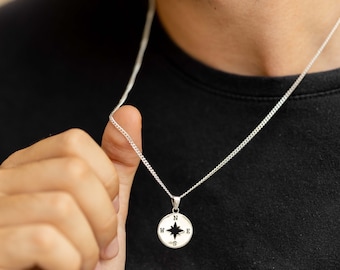 May include: A silver chain necklace with a compass pendant. The compass has a black star in the centre and the letters N, S, E, and W around the edge.