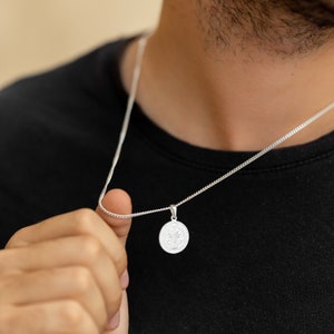 May include: A silver chain necklace with a round pendant featuring a religious figure. The pendant is detailed with intricate designs.