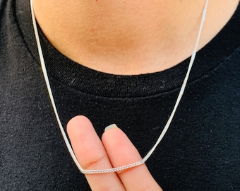 May include: A silver chain necklace with a delicate, thin design. The chain is shown being held by a finger.