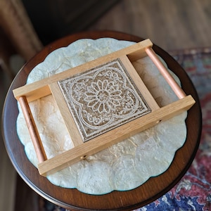 Peut inclure: Un plateau de service en bois avec des poignées en cuivre et un carrelage décoratif encastré. Le carrelage est brun avec un motif floral blanc.