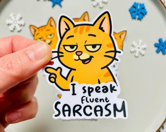 May include: A sticker of an orange cartoon cat with a sarcastic expression, pointing with its paw. The text "I speak fluent SARCASM" is below the cat. The sticker is held against a plate decorated with snowflakes.