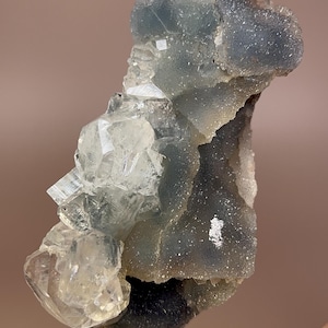 May include: A cluster of translucent, light blue and clear quartz crystals. The crystals have a rough, textured appearance and are arranged in a layered formation. The overall shape is irregular, with sharp edges and points.