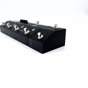 May include: Black foot pedal with five buttons labeled 1 through 4. The buttons are silver and have a black rubber top. The pedal has a black textured surface and the text "OCD" is embossed on the side.