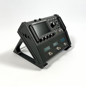 Può includere: Processore audio digitale nero con schermo, pulsanti e manopole, montato su un supporto nero. Il dispositivo presenta la scritta "FM3 MARK II AMP MODELER/FX PROCESSOR". Progettato per l'elaborazione audio e gli effetti.