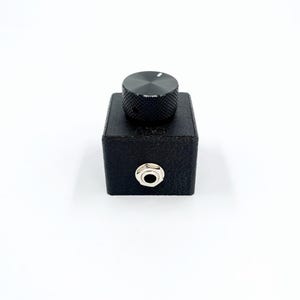 Könnte beinhalten: Eine schwarze Box mit einem einzigen Knopf und einer 6,35 mm Klinkenbuchse. Die Box ist aus einem strukturierten Material.