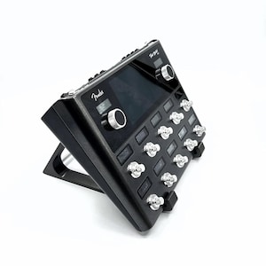 May include: A black Fender Tone Master Amp with a digital display and 12 footswitches. The amp is angled on a stand.