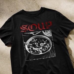 Puede incluir: Camiseta negra con un gráfico blanco de un tazón de sopa y la palabra "SOUP" en letras rojas.