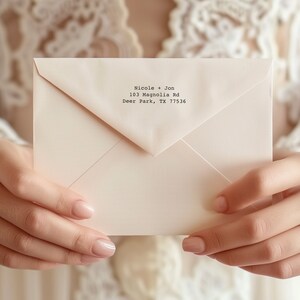 May include: A pale pink envelope featuring black printed text that reads Nicole + Jon, 103 Magnolia Rd, Deer Park, TX 77536. The envelope has a triangular flap and a smooth, matte finish, presented in a clean, simple, and professional style.