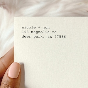May include: A cream-colored rectangular card featuring black typewriter-style text that reads: nicole + jon, 103 magnolia rd, deer park, tx 77536. The card has a clean, smooth surface and is presented with a simple, minimalist aesthetic.