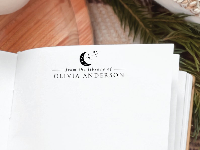 May include: A white book with a black and white crescent moon and stars design. The text "from the library of" and "OLIVIA ANDERSON" is printed below the design.