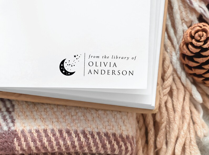 May include: A white book with a black and white stamp that reads "from the library of Olivia Anderson". The stamp features a crescent moon with stars.