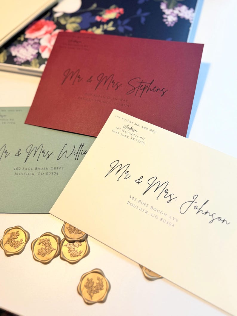 K&ouml;nnte beinhalten: Drei Hochzeitseinladungen mit kalligrafischen Namen und Adressen. Die Umschl&auml;ge sind in Rot-, Gr&uuml;n- und Cremet&ouml;nen gehalten. Die Umschl&auml;ge sind mit goldenen Siegellacken verziert.