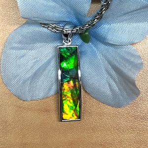 May include: A silver pendant necklace with a rectangular green, yellow, and orange gemstone.