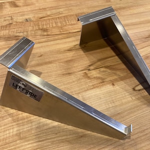 Op de afbeelding: Twee zilveren metalen beugels, een met het label "LEFT SIDE". De beugels zijn schuin en hebben een rechthoekige vorm.