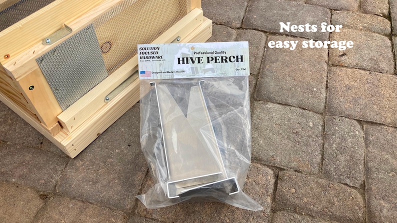 Op de afbeelding: Een zilveren metalen bijenkorf-zitstok voor imkerij. De zitstok is ontworpen om te worden gebruikt met een bijenkorf en is gemaakt van duurzaam metaal. De verpakking vermeldt "Professional Quality Hive Perch".