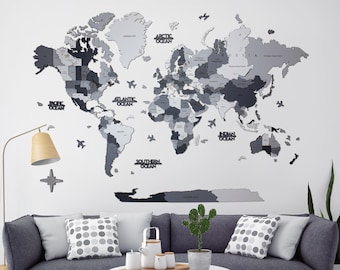 May include: A gray and white wooden world map with the names of the oceans printed on it. The map is mounted on a white wall above a gray couch with pillows. A white coffee table with a wooden tray and a cactus plant are in front of the couch.