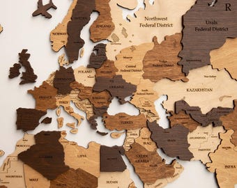 May include: A wooden world map with countries cut out and labeled. The map features various shades of brown and tan wood, with country names visible. An airplane-shaped wooden cutout is placed near the word "OCEAN".