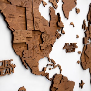May include: A wooden world map with a focus on North America. The map is made of individual pieces of wood that are assembled together. The map is labeled with the names of the states and provinces. The map is a light brown color and has a natural wood finish.