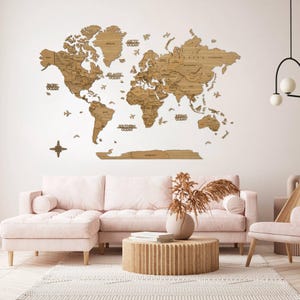 Peut inclure: Une grande carte du monde en bois fixée au mur. La carte, en bois brun clair, présente les contours des pays et les noms des océans. Elle est au-dessus d'un canapé rose et d'une table basse ronde en bois.
