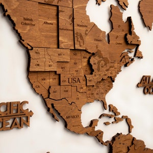 May include: A wooden world map puzzle with the North American continent assembled. The map is made of light brown wood and features the names of each state and province. The map is on a white background.