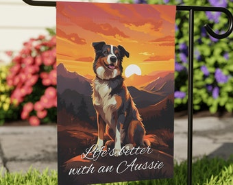 Peut inclure: Un drapeau de jardin avec un fond de coucher de soleil et un chien australien berger brun et noir assis sur un rocher. Le texte "Life's better with an Aussie" est imprimé sur le drapeau.
