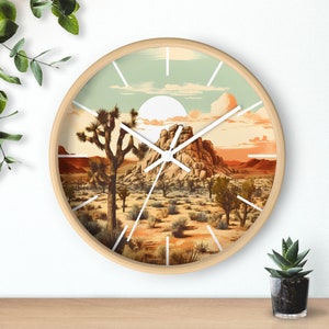 May include: A round wall clock with a white face and black hands. The clock face features a desert landscape with a large rock formation, Joshua trees, and a blue sky with clouds. The clock is made of wood and has a light brown finish.