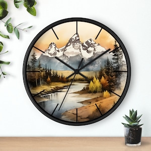 May include: A black framed clock with a watercolor mountain scene. The clock face features black hands and Roman numeral markings. The scene depicts a mountain range with a river flowing through the valley. The mountains are snow-capped and the river is a light blue color. The background is a soft yellow and orange gradient.