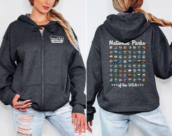 May include: A dark charcoal gray zip-up hoodie featuring a small National Parks of the USA logo on the front left chest. The back displays a grid of colorful National Parks emblems with the text National Parks of the USA below it.