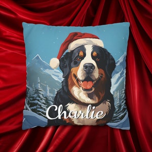 May include: Square throw pillow featuring a Bernese Mountain Dog wearing a Santa hat. The dog is set against a winter mountain scene with the name "Charlie" in white script. The pillow has a blue background.