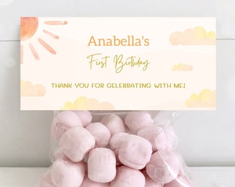 May include: A white favor bag with a watercolor design of a sun and clouds. The bag has a label that says "Anabella's First Birthday" and "Thank you for celebrating with me!"